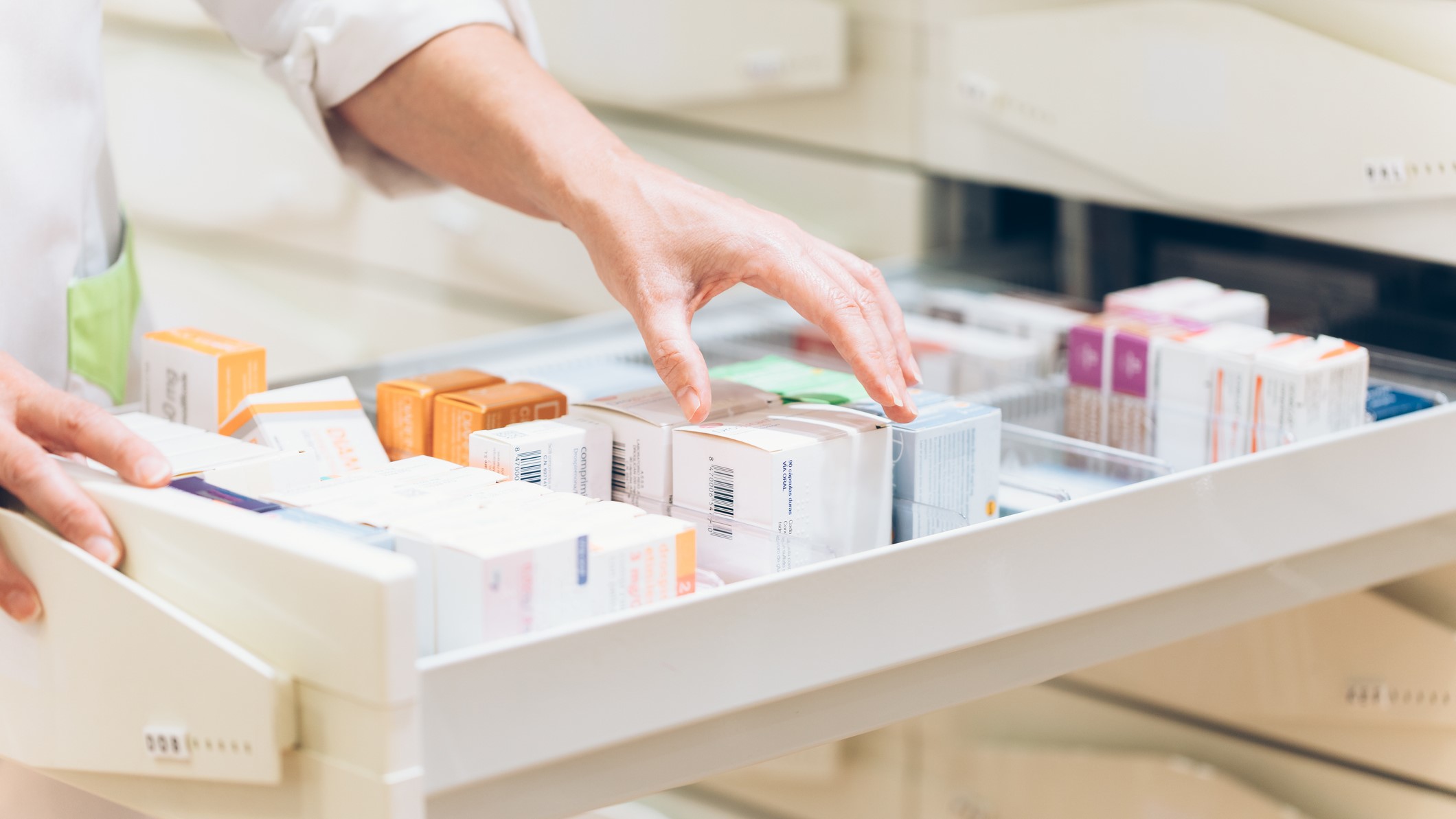 Una farmaceútica cogiendo los medicamentos de un cliente de un cajón.
